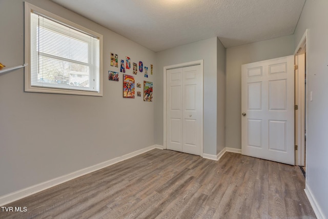 unfurnished bedroom with a closet, baseboards, a textured ceiling, and wood finished floors