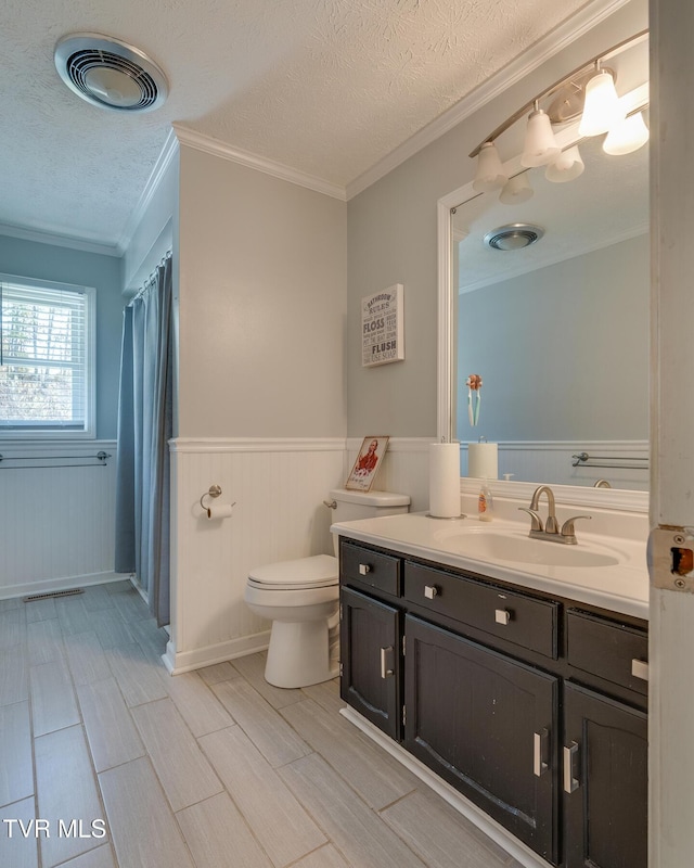 bathroom featuring visible vents, toilet, a wainscoted wall, and a textured ceiling