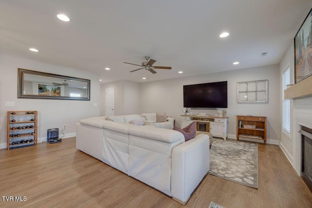 living room featuring recessed lighting, a fireplace, baseboards, and light wood finished floors