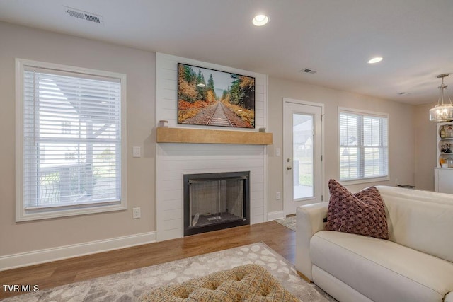 living area featuring recessed lighting, a large fireplace, a healthy amount of sunlight, and wood finished floors