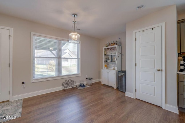 unfurnished dining area featuring a dry bar, wood finished floors, and baseboards