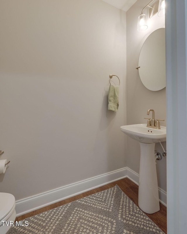 half bathroom featuring baseboards, toilet, and wood finished floors