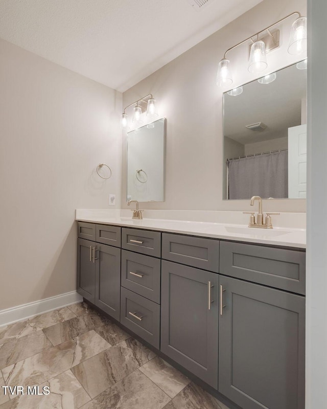 bathroom with double vanity, baseboards, marble finish floor, and a sink