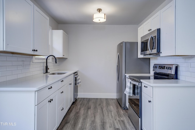 kitchen with baseboards, light countertops, wood finished floors, stainless steel appliances, and a sink