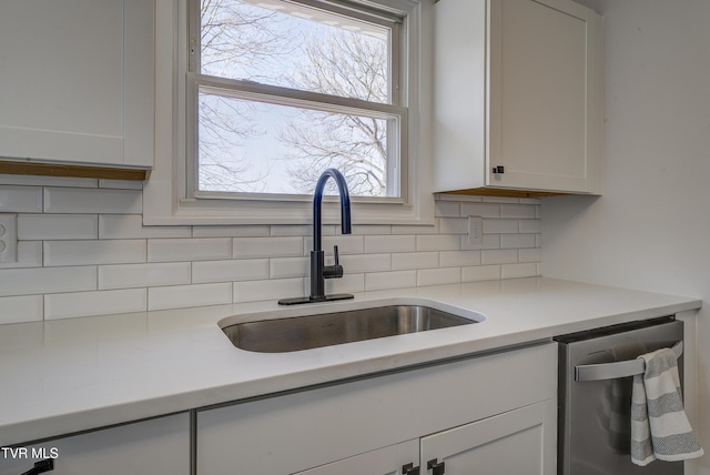 kitchen featuring a sink, stainless steel dishwasher, white cabinetry, light countertops, and decorative backsplash