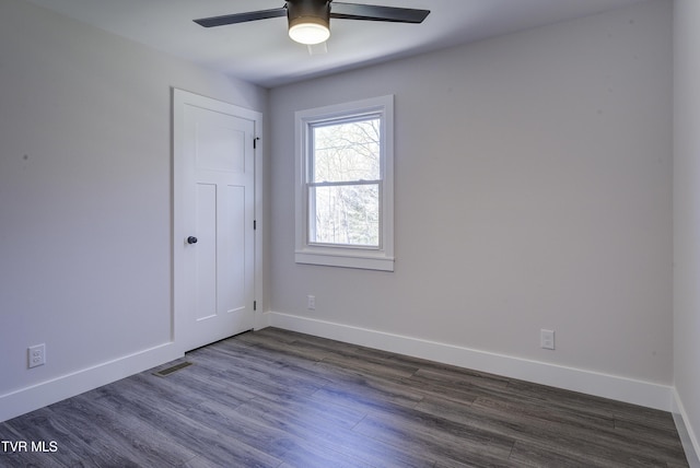 unfurnished room with dark wood-style floors, visible vents, a ceiling fan, and baseboards