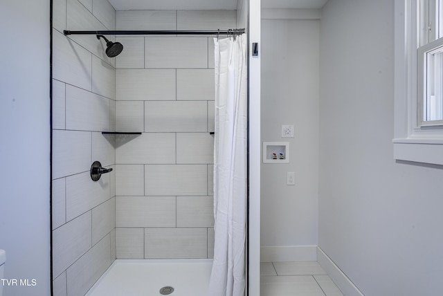 full bathroom with toilet, tiled shower, and baseboards