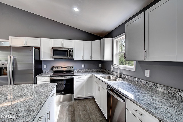 kitchen with a sink, appliances with stainless steel finishes, dark wood finished floors, vaulted ceiling, and light stone countertops