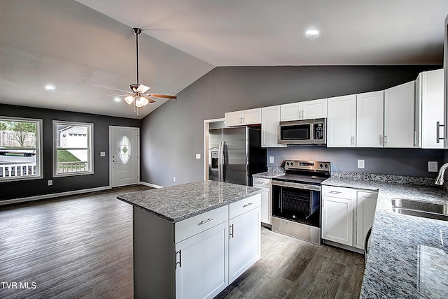 kitchen with a sink, dark wood-style flooring, vaulted ceiling, light stone countertops, and stainless steel appliances