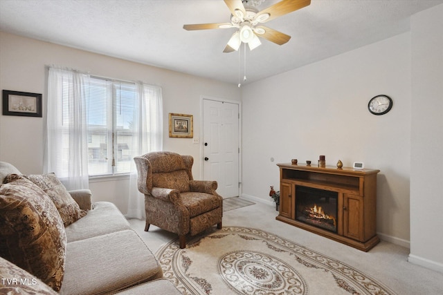 living area with a glass covered fireplace, light colored carpet, baseboards, and ceiling fan