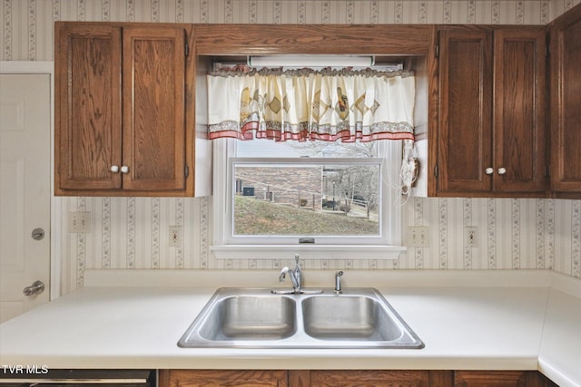 kitchen with brown cabinetry, wallpapered walls, light countertops, and a sink