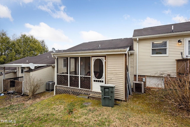 rear view of house featuring central AC unit, a shingled roof, a yard, and a sunroom