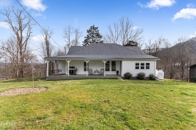 back of house featuring a chimney, covered porch, a lawn, and metal roof