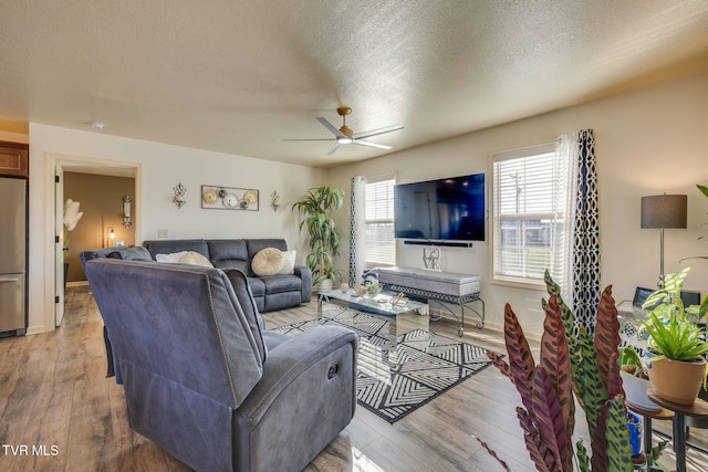 living area with light wood-type flooring, baseboards, a textured ceiling, and ceiling fan