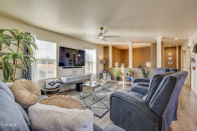 living area with ceiling fan, a textured ceiling, light wood-style flooring, and ornate columns