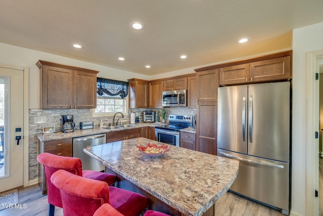 kitchen with tasteful backsplash, a center island, light wood-style flooring, appliances with stainless steel finishes, and a sink