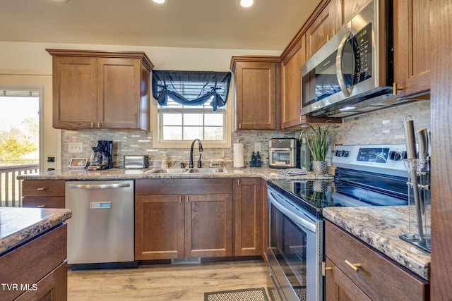 kitchen with light stone countertops, a sink, light wood-style floors, appliances with stainless steel finishes, and tasteful backsplash