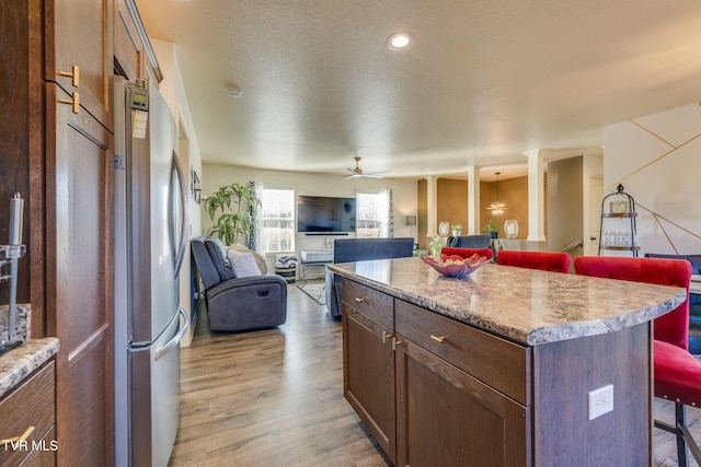 kitchen featuring wood finished floors, decorative columns, freestanding refrigerator, a kitchen bar, and a center island