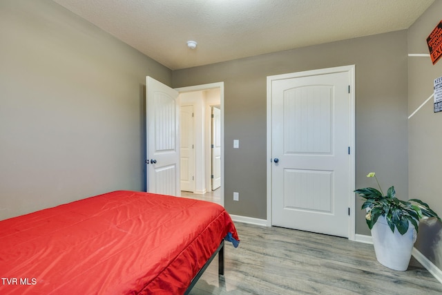 bedroom featuring baseboards, a textured ceiling, and wood finished floors