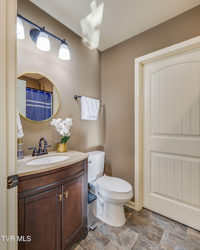 bathroom with a textured ceiling, toilet, vanity, and stone finish floor