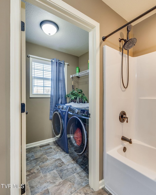 bathroom with stone finish floor, a textured ceiling, shower / bathing tub combination, baseboards, and washing machine and clothes dryer