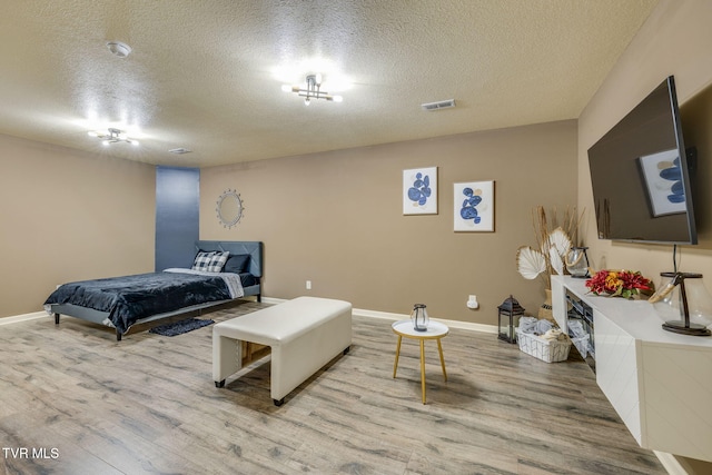 bedroom featuring visible vents, a textured ceiling, baseboards, and wood finished floors