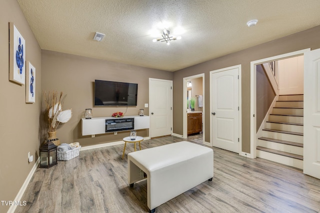 living area with stairs, wood finished floors, visible vents, and a textured ceiling