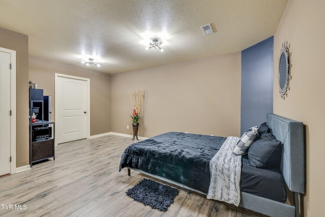 bedroom with baseboards, wood finished floors, visible vents, and a textured ceiling