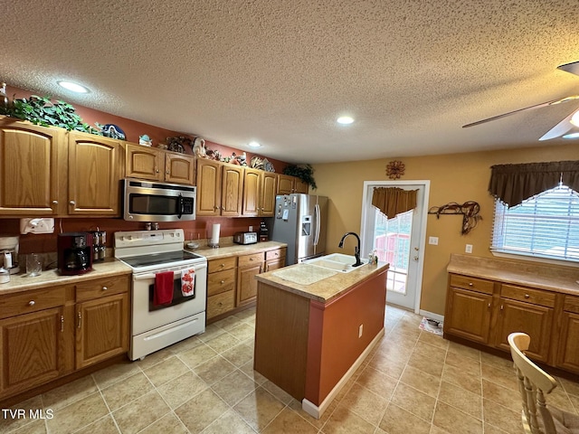 kitchen with ceiling fan, an island with sink, light countertops, brown cabinets, and stainless steel appliances