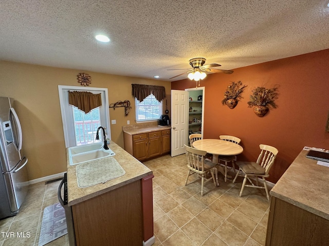 kitchen with ceiling fan, a sink, light countertops, stainless steel refrigerator with ice dispenser, and a textured ceiling