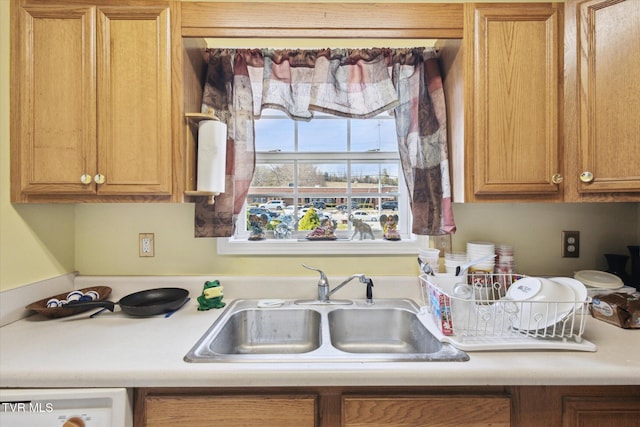 kitchen featuring a sink, white dishwasher, brown cabinetry, and light countertops