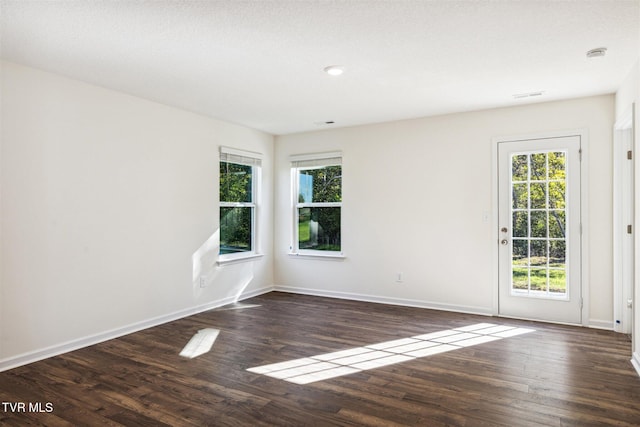 empty room with dark wood finished floors, a healthy amount of sunlight, and baseboards