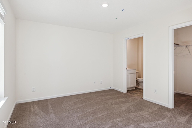 unfurnished bedroom with a walk in closet, baseboards, a closet, and carpet floors