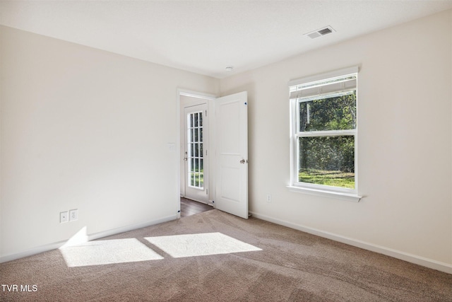 carpeted empty room with a healthy amount of sunlight, visible vents, and baseboards