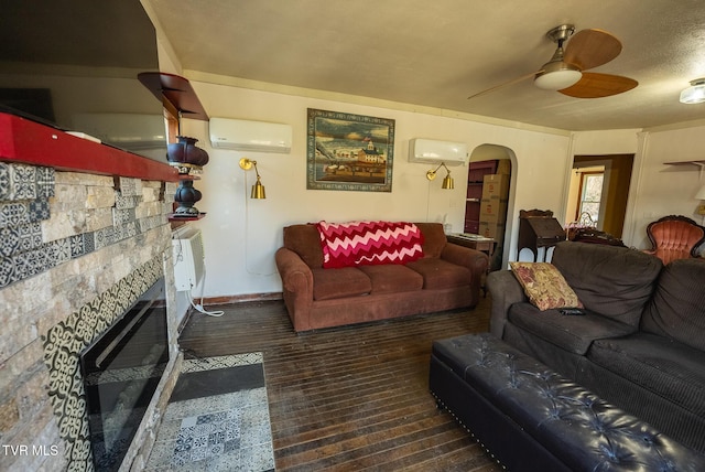 living room featuring arched walkways, an AC wall unit, a stone fireplace, and ceiling fan