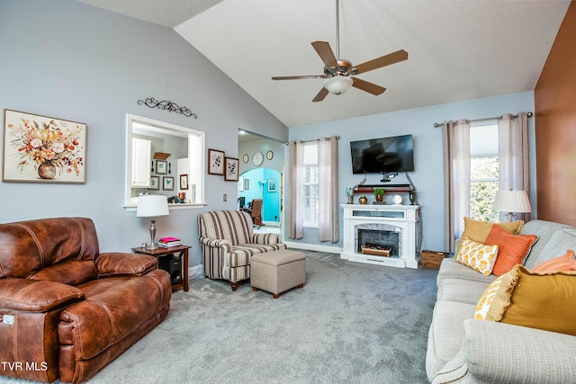 carpeted living room featuring high vaulted ceiling, a fireplace with raised hearth, baseboards, and ceiling fan