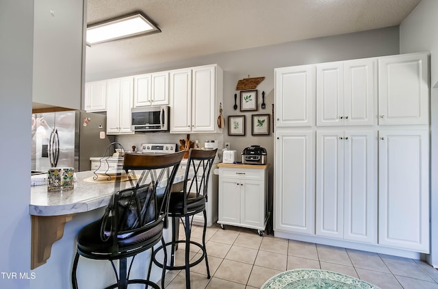 kitchen featuring a kitchen bar, light countertops, light tile patterned floors, and stainless steel appliances