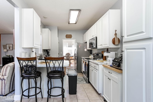 kitchen featuring a peninsula, appliances with stainless steel finishes, a breakfast bar area, white cabinets, and light tile patterned floors