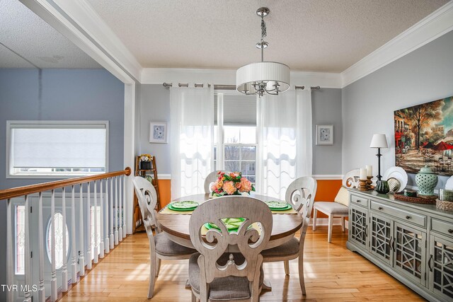 dining area featuring a textured ceiling, a notable chandelier, light wood-style floors, and ornamental molding