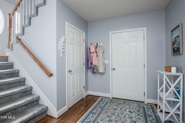 foyer entrance featuring a textured ceiling, stairs, baseboards, and dark wood-style flooring