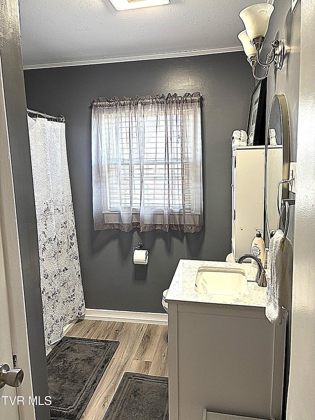 bathroom with baseboards, wood finished floors, ornamental molding, and vanity