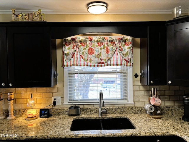 kitchen with crown molding, tasteful backsplash, dark cabinets, and a sink