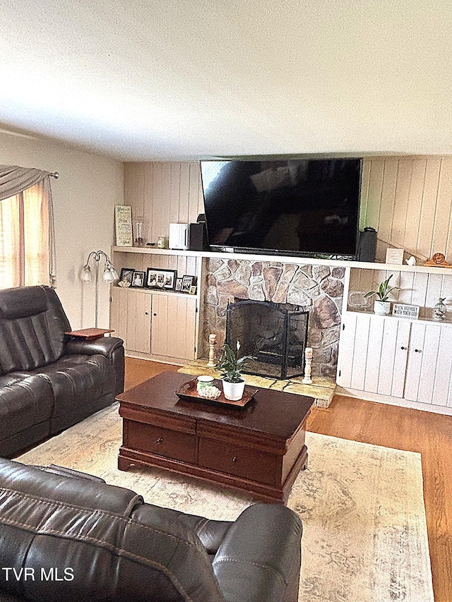 living area with a textured ceiling, a stone fireplace, and wood finished floors