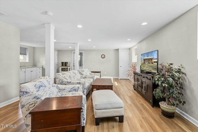 living room with decorative columns, light wood-style floors, recessed lighting, and baseboards