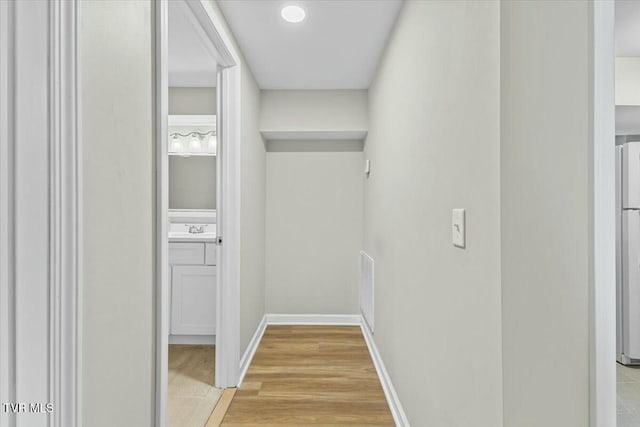 hallway with visible vents, baseboards, light wood-type flooring, and a sink