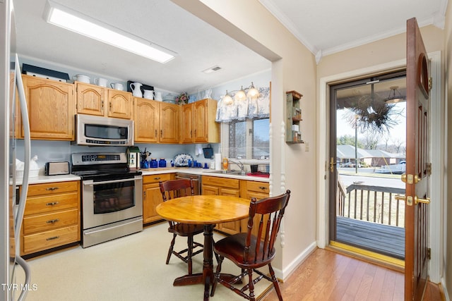 kitchen with a sink, stainless steel appliances, light countertops, crown molding, and light wood-type flooring