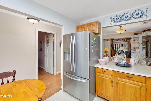 kitchen featuring visible vents, light wood finished floors, ornamental molding, light countertops, and stainless steel fridge