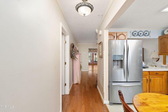 kitchen with stainless steel fridge with ice dispenser, light countertops, ornamental molding, light wood-style floors, and a textured ceiling