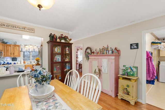 dining room with a textured ceiling, crown molding, light wood finished floors, and washer / dryer