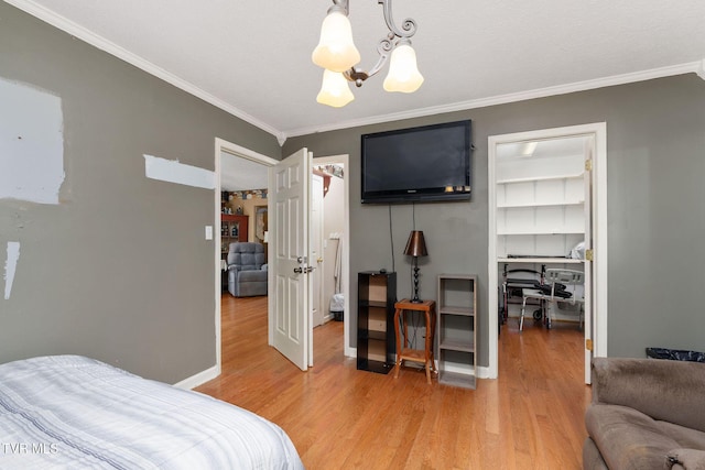 bedroom featuring light wood finished floors, a spacious closet, crown molding, baseboards, and a chandelier